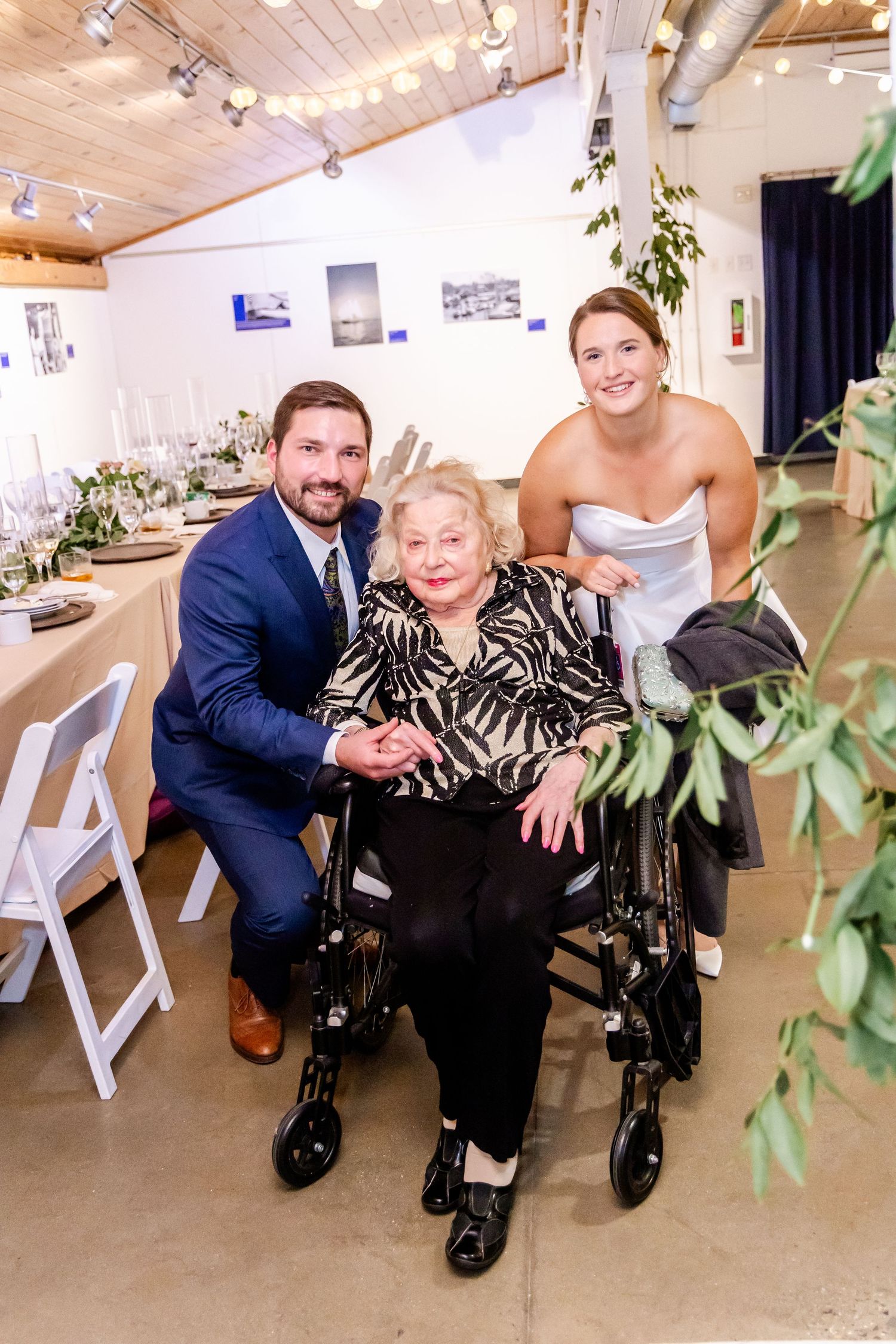 Bride and groom posing with elderly woman in wheelchair at elegant wedding reception venue.