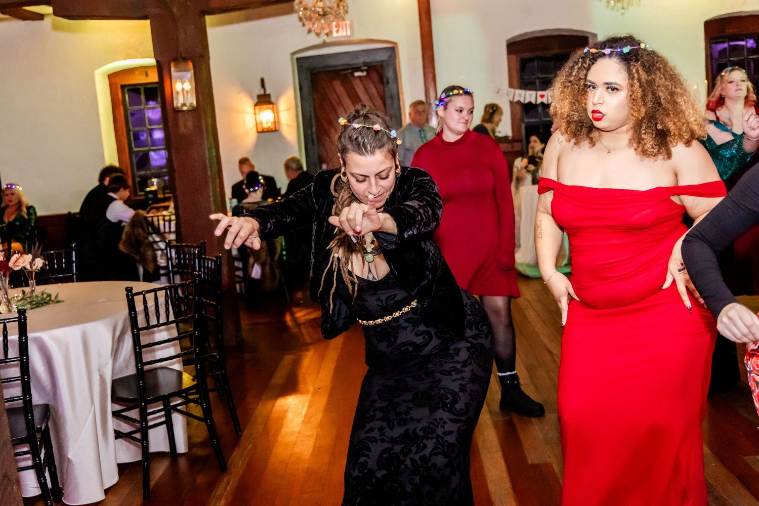 Wedding guests dancing and mingling in an elegant venue with hardwood floors and warm lighting.