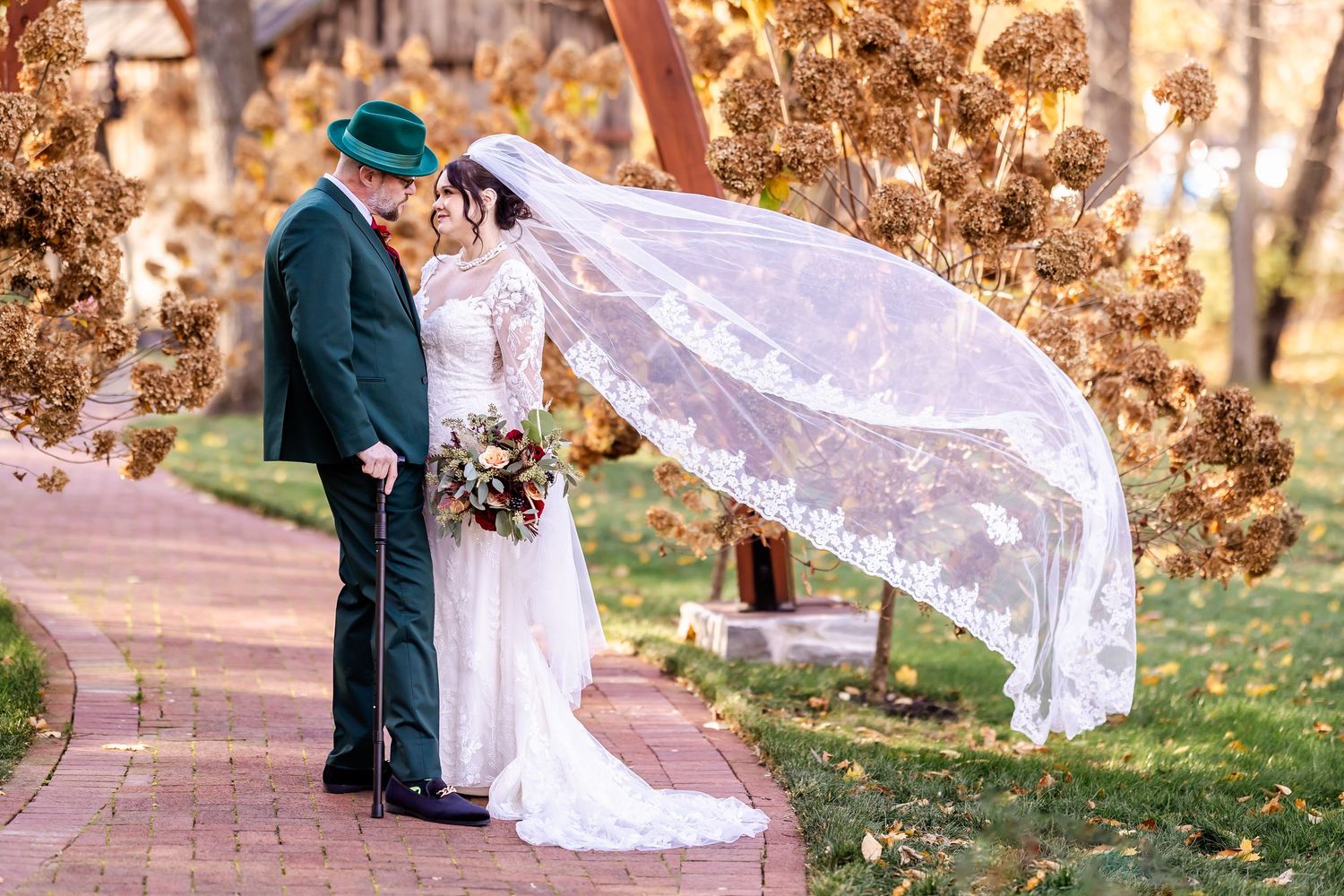 A romantic wedding photo with a flowing lace veil caught in the autumn breeze along a garden path.
