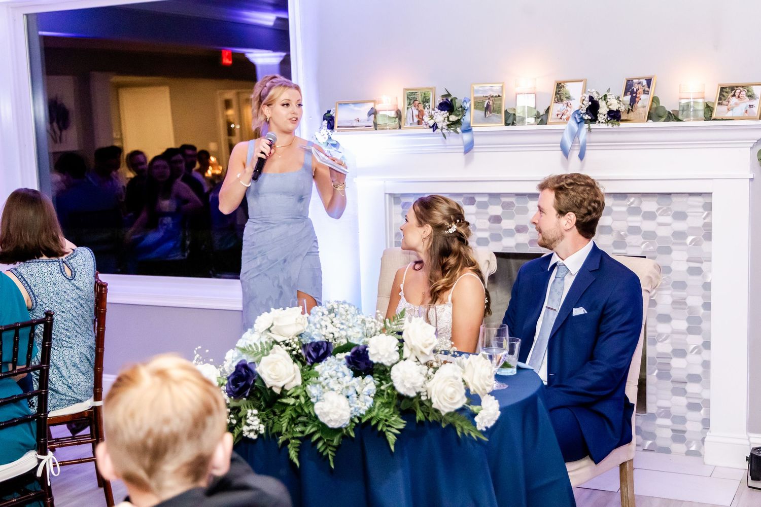 Wedding reception toast with elegant white floral centerpieces and mantle decor.