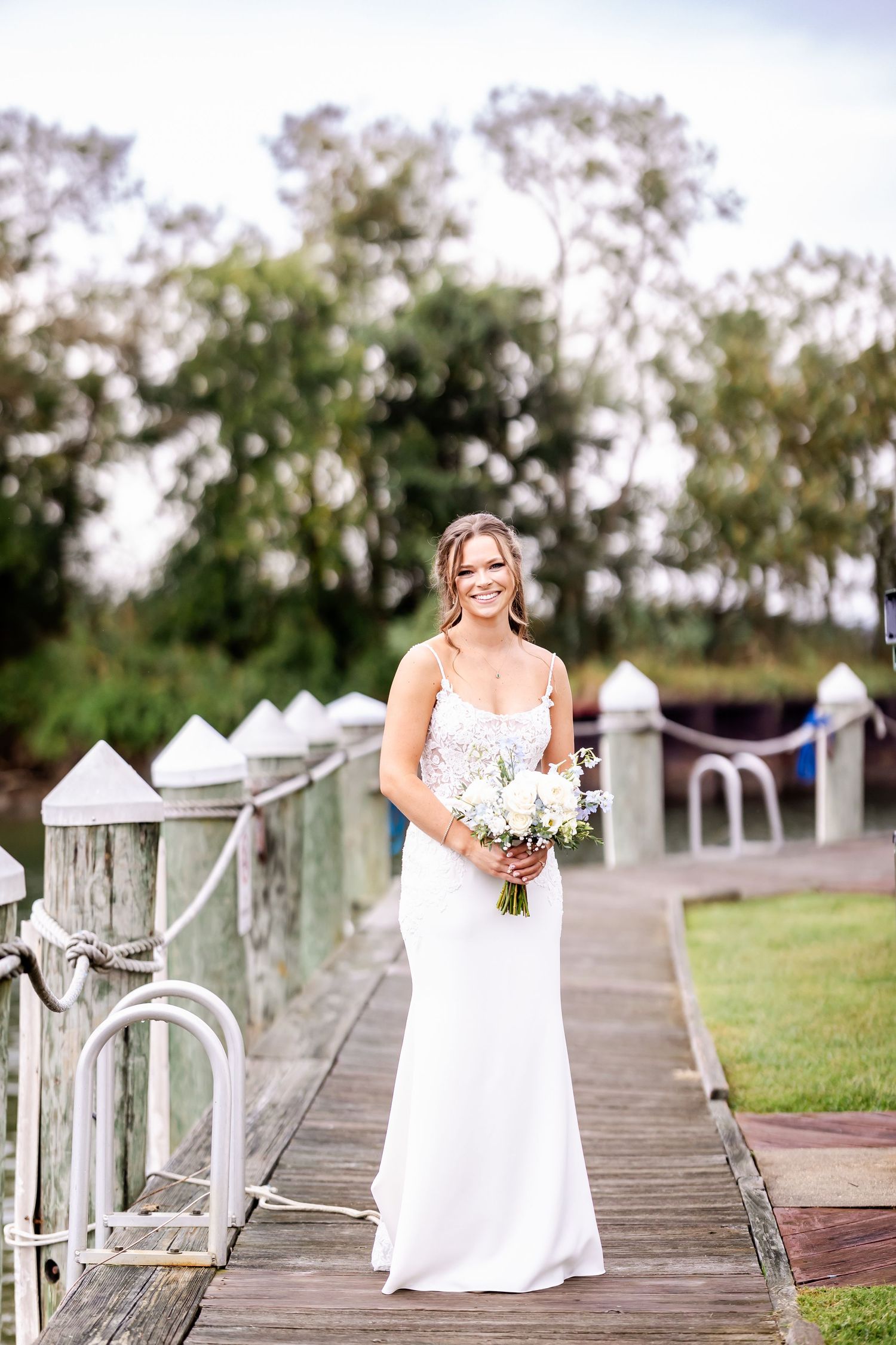 White wooden boardwalk decorated with wedding decor and lanterns leading to a waterfront venue.
