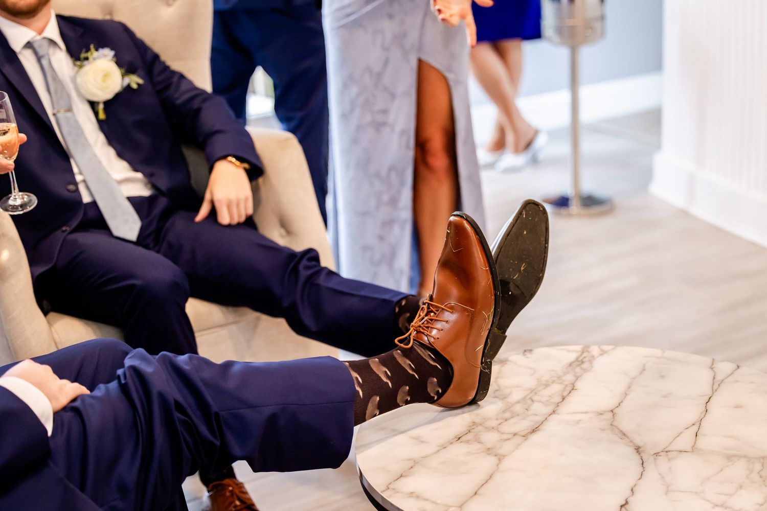Wedding party members' feet and shoes shown while sitting on white surface.