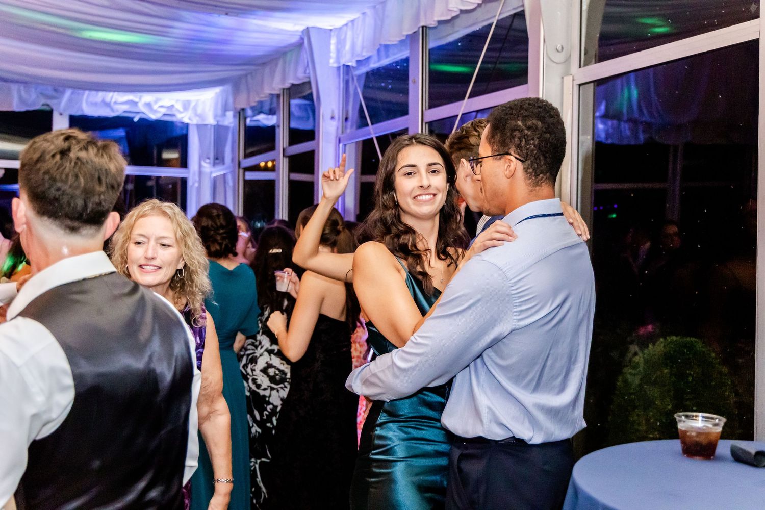 Wedding guests dancing under purple mood lighting at evening reception.