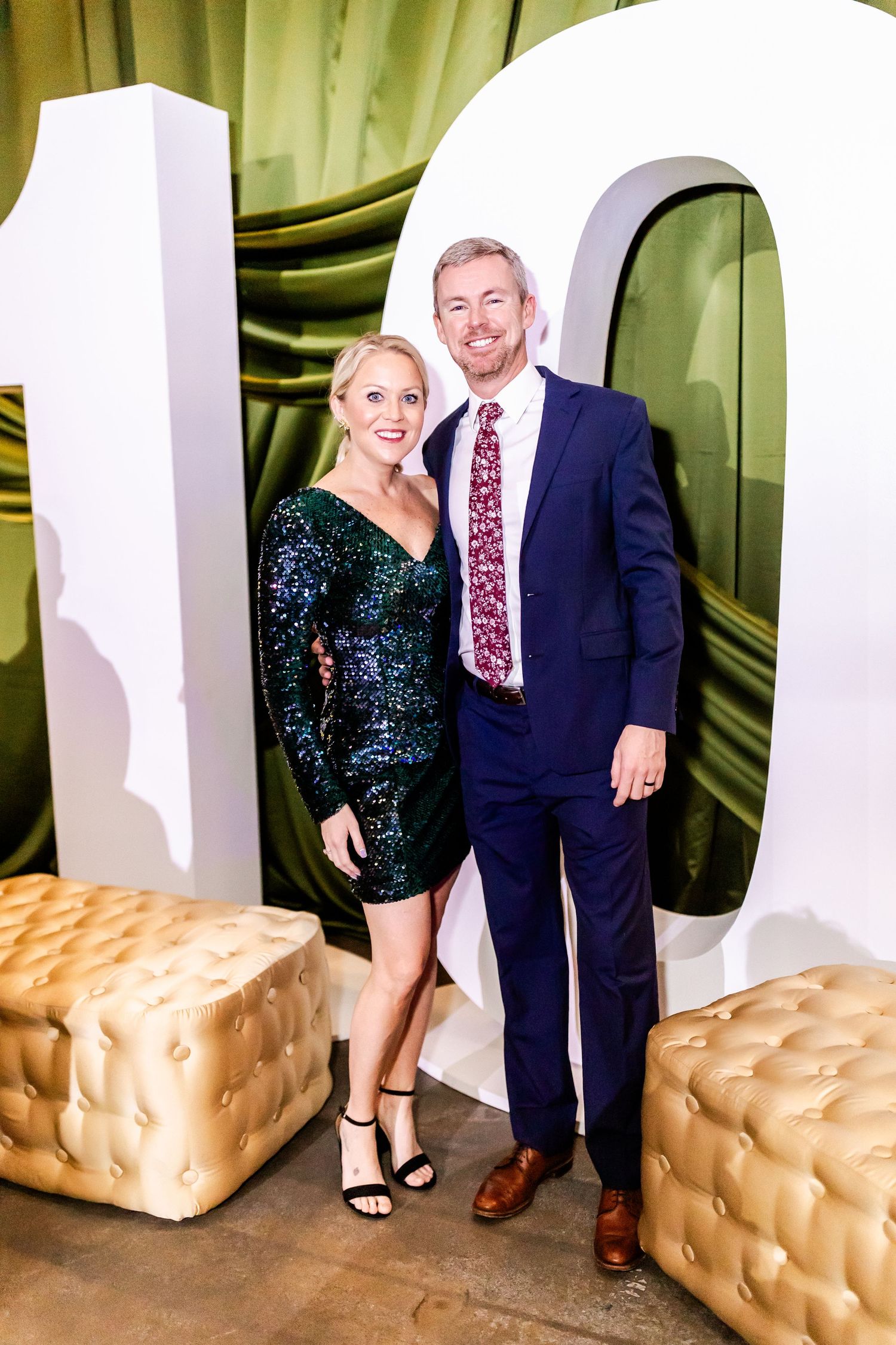 Couple poses in formal attire against a white decorative backdrop with gold cushioned cubes.