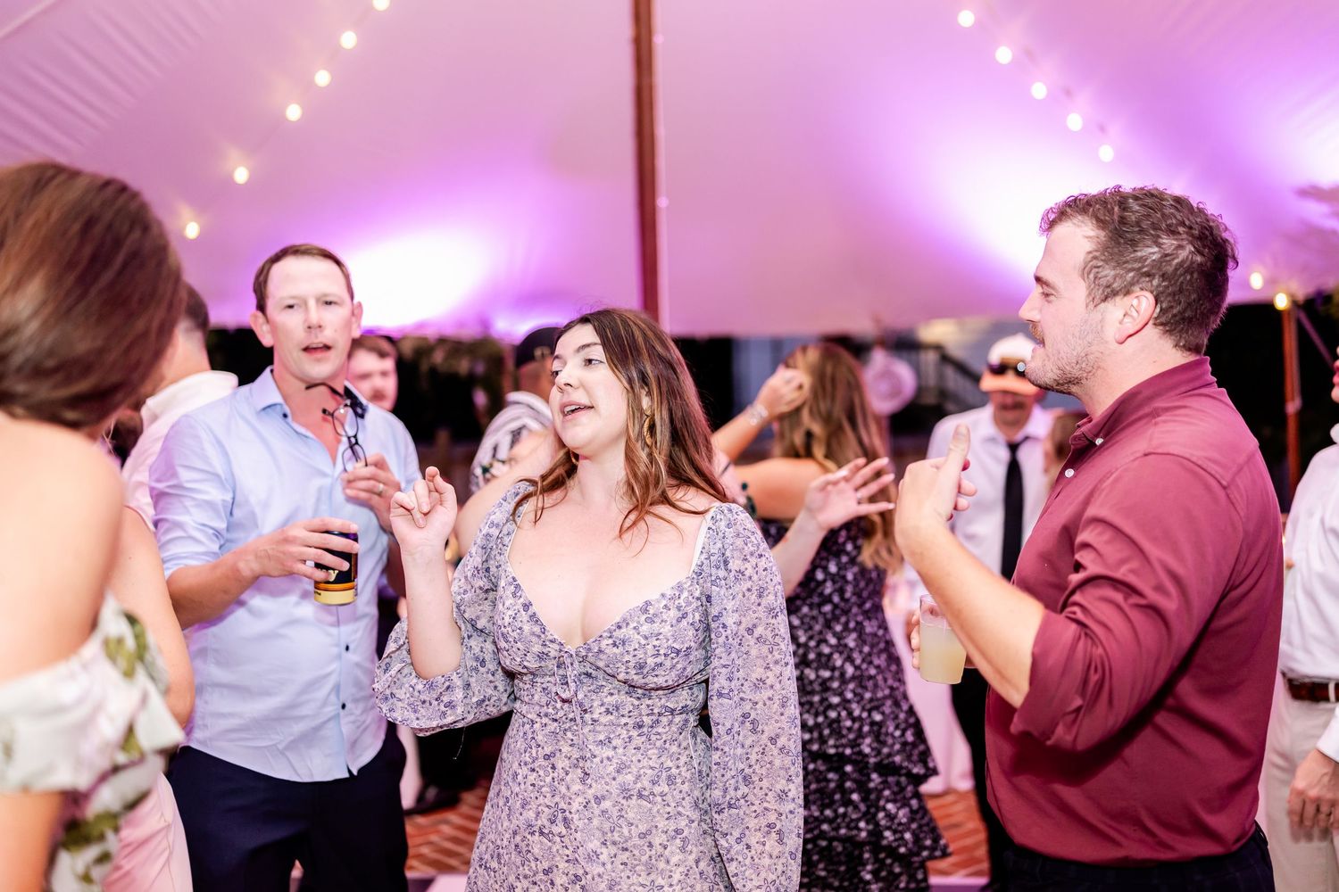 Wedding reception dance floor filled with guests enjoying celebration under purple lighting.