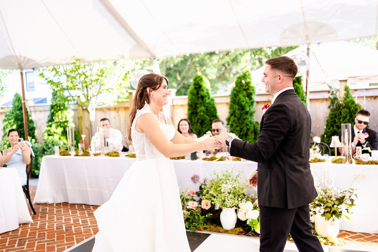 Outdoor wedding reception setup with white tents and tables on a patio.