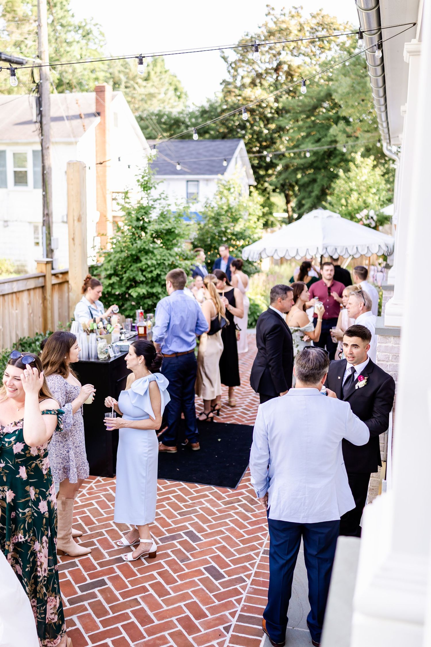 Guests mingle during an outdoor cocktail reception on a brick patio under a white tent.