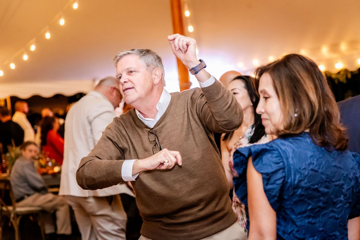 Wedding guests enjoy dancing and celebrating on the dance floor under warm tent lighting.