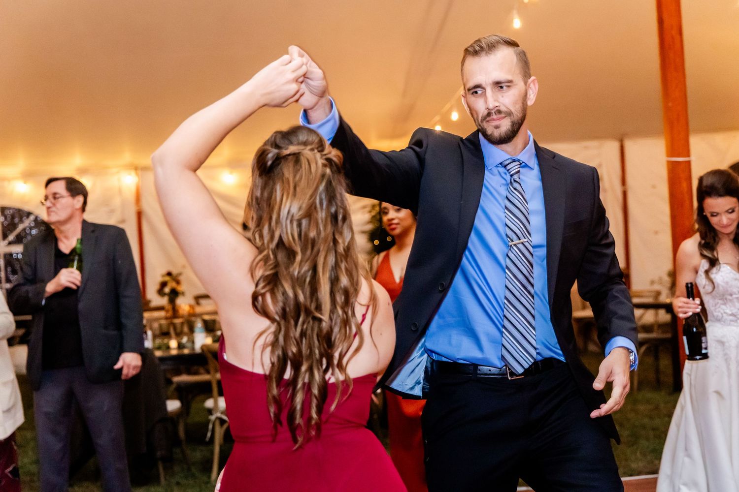 Couples dancing under a reception tent with warm lighting.