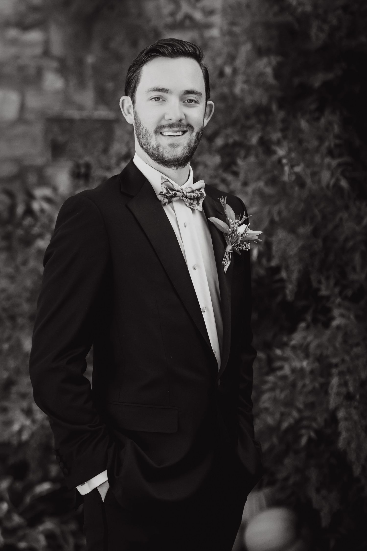 Formal wedding portrait of groom in black tuxedo and bow tie with boutonniere.