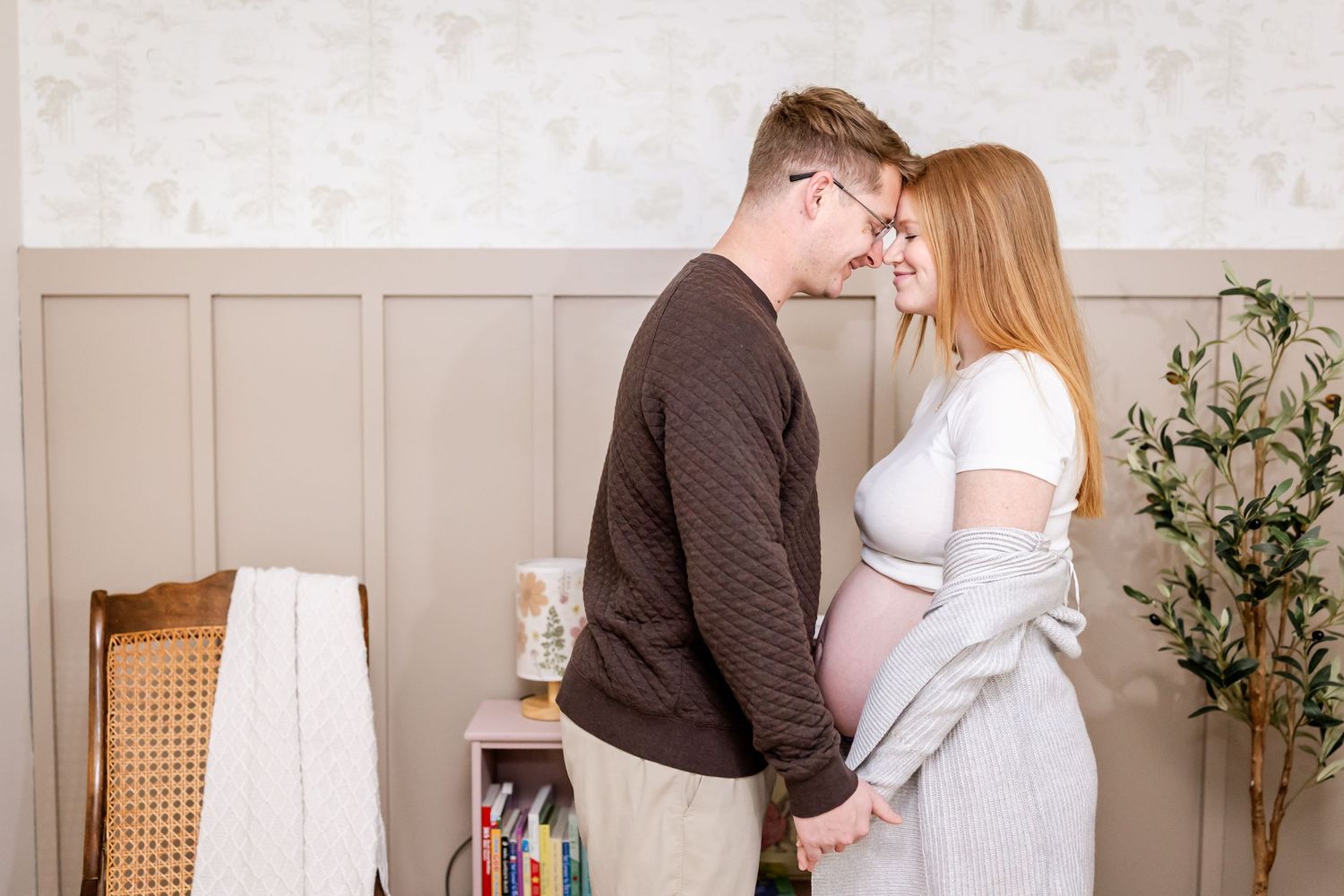Intimate maternity photo of couple embracing in neutral-toned nursery setting.