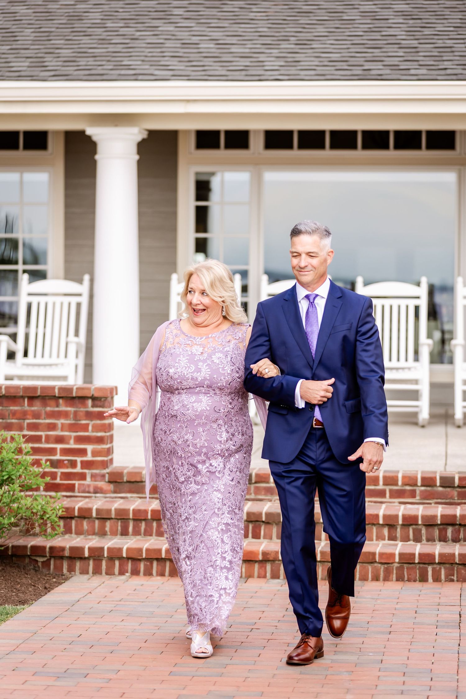 Couple walking together on brick pathway, with woman in sparkly lavender dress and man in navy suit.