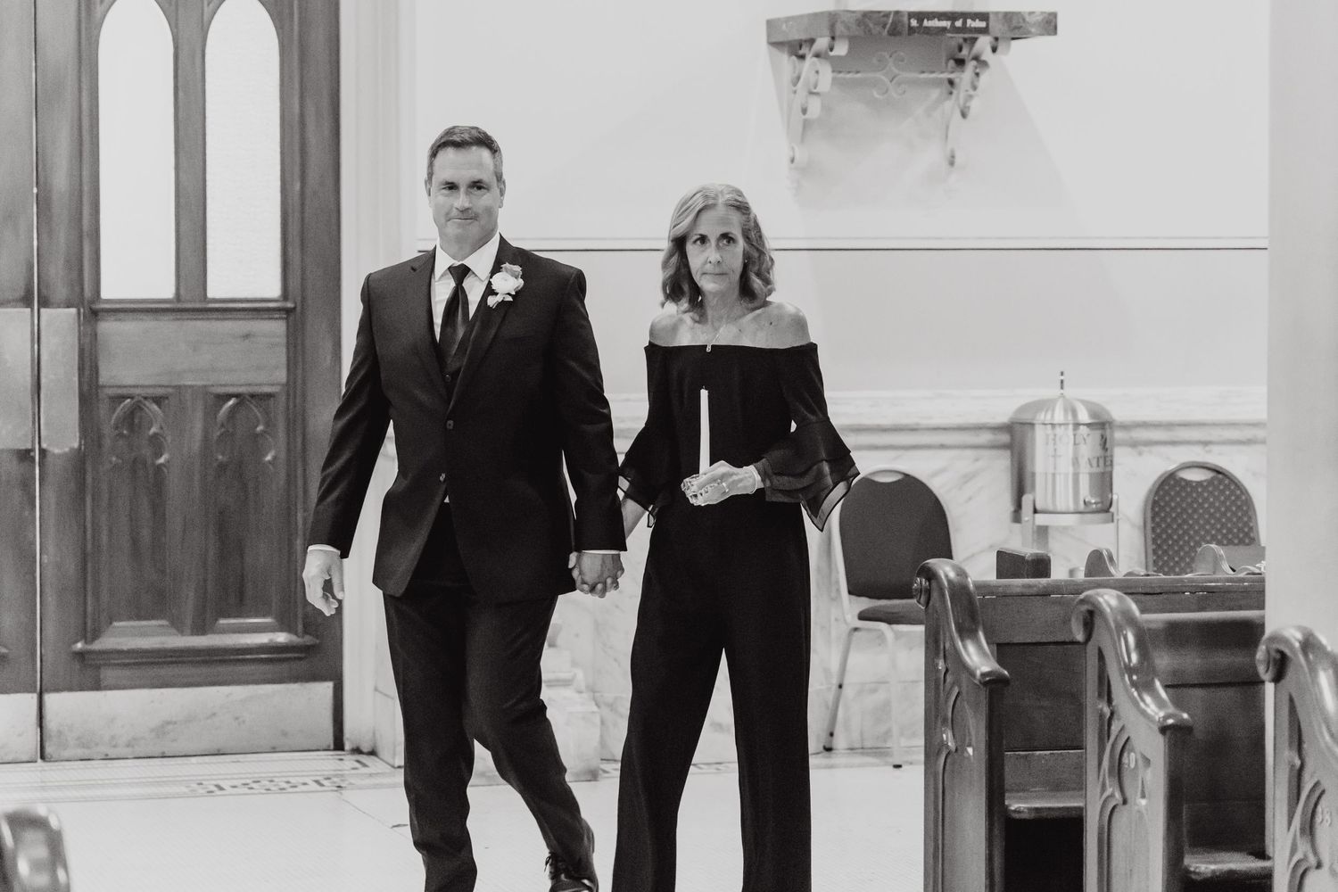 Wedding party members walking in formal attire through a church hallway.