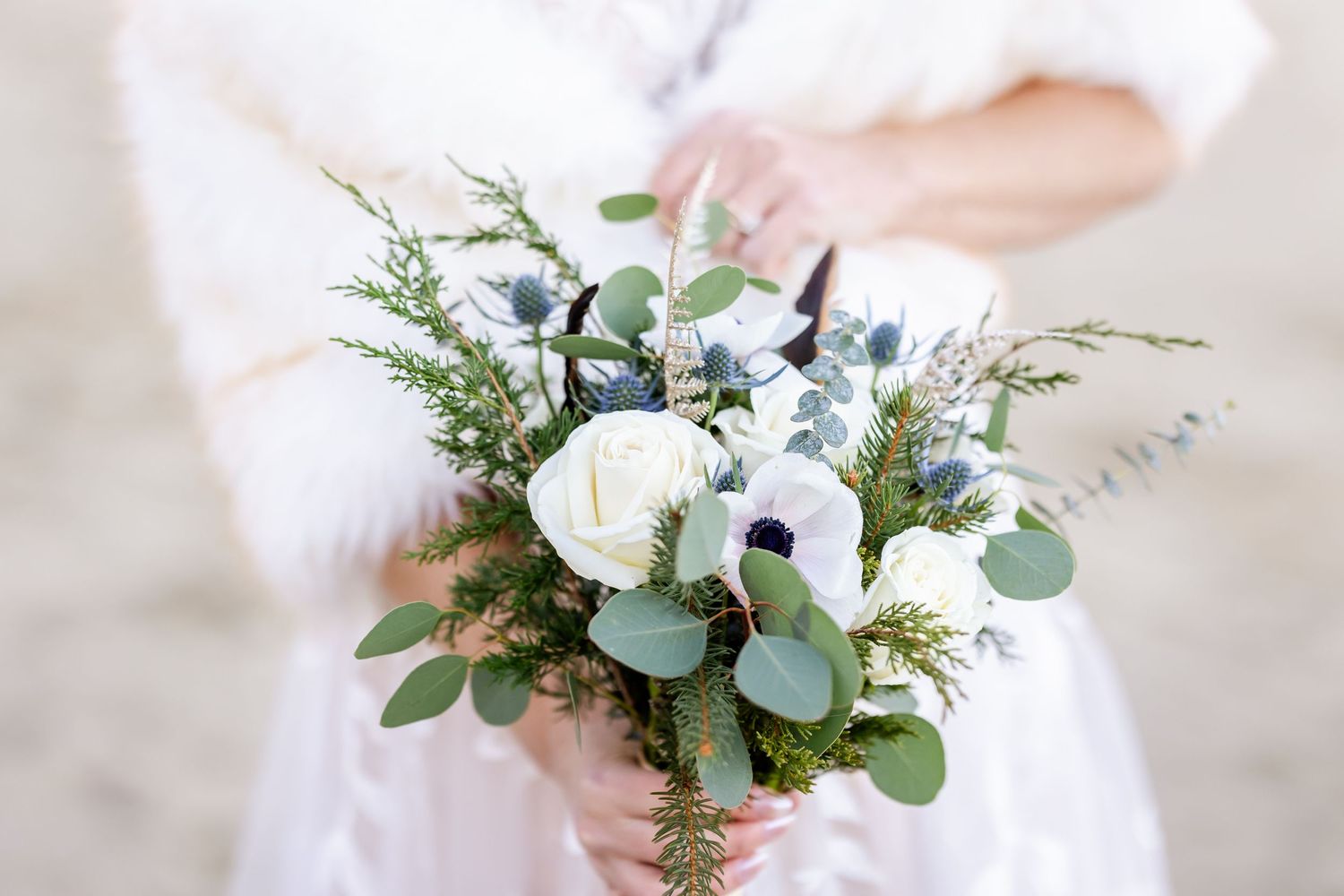 A delicate winter wedding bouquet with white anemones, eucalyptus, and blue thistle.