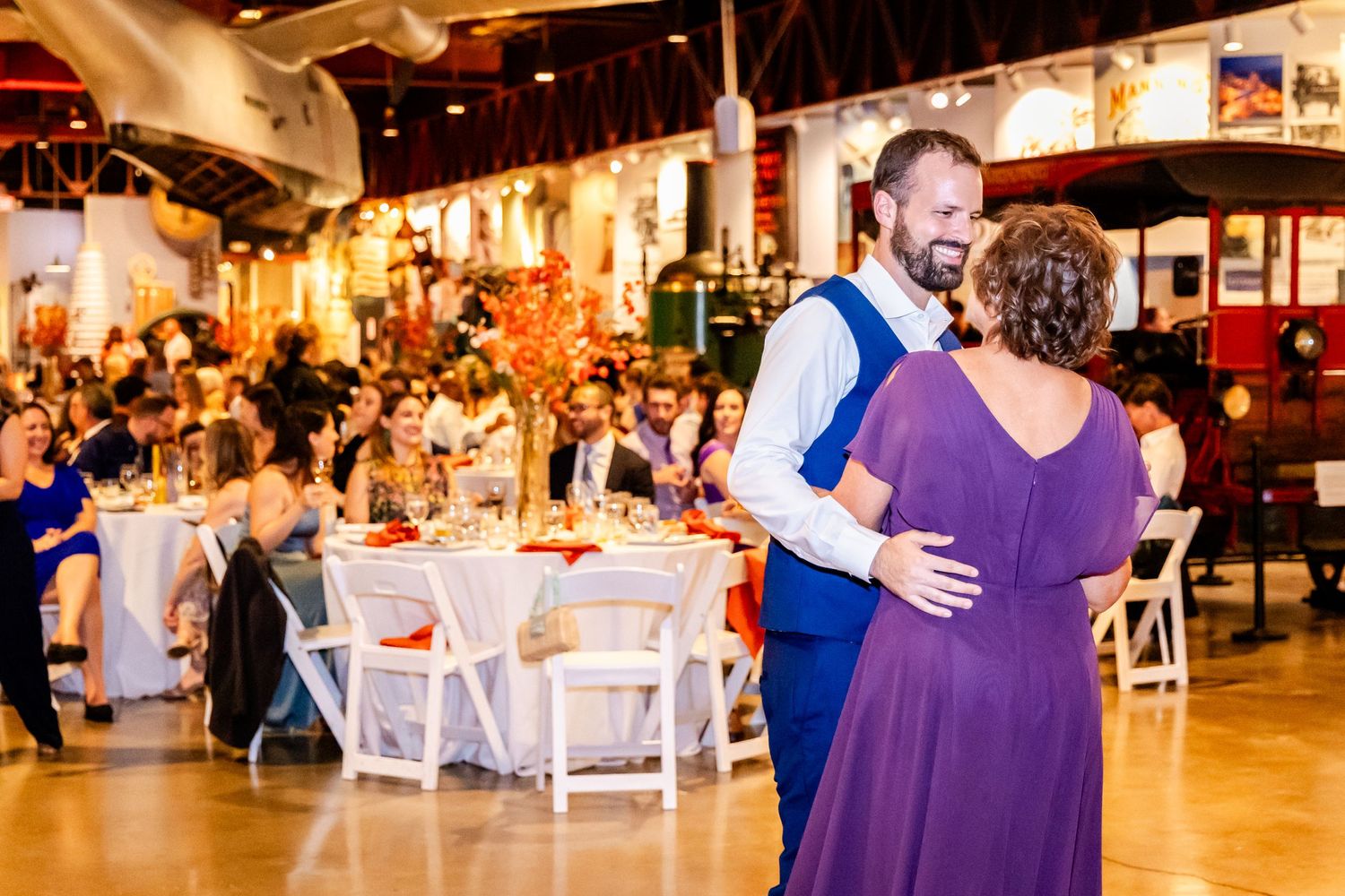 A dance floor moment at a wedding reception with purple and white decor in an indoor venue.
