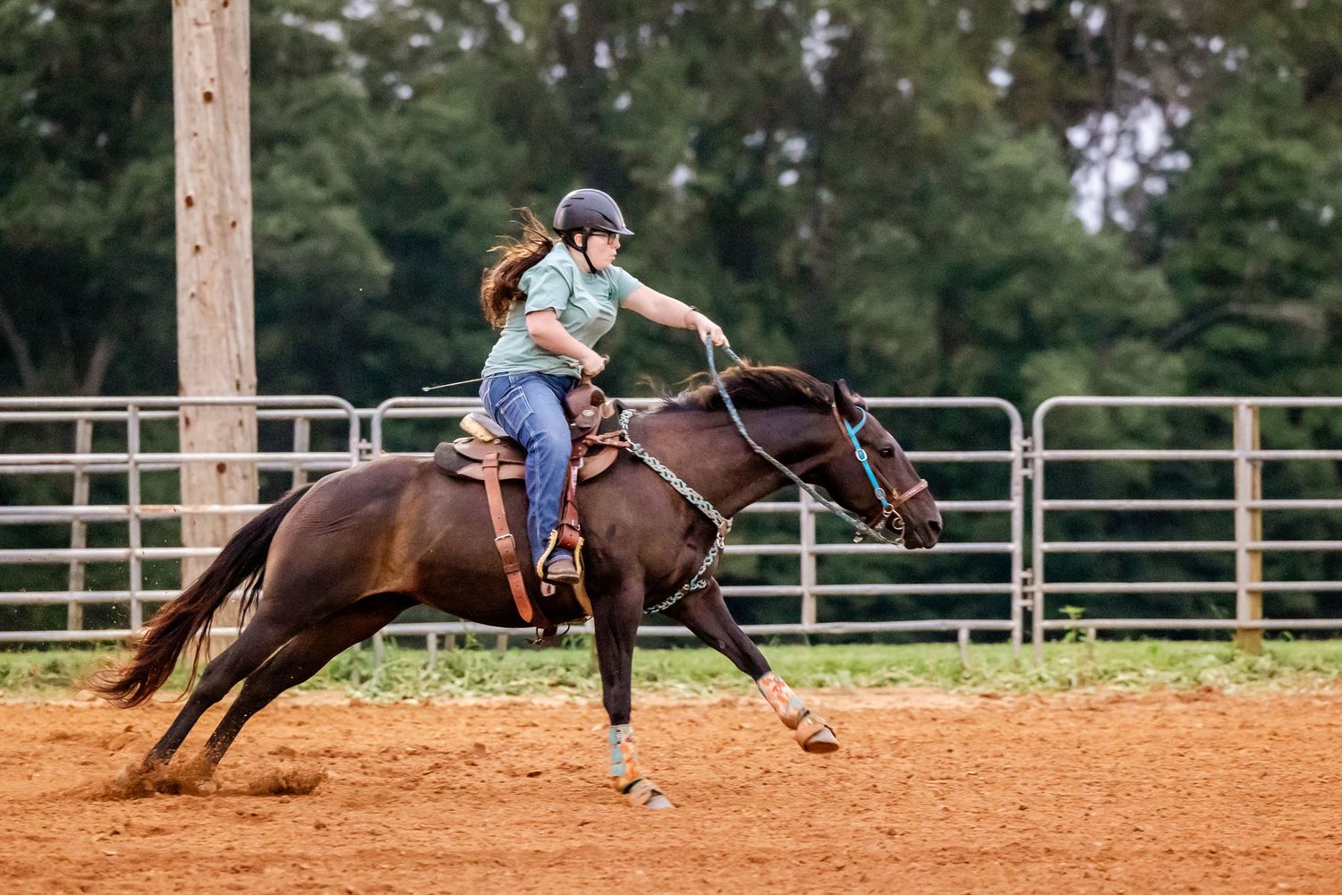 Rider on dark horse performing sliding stop maneuver in dirt arena.
