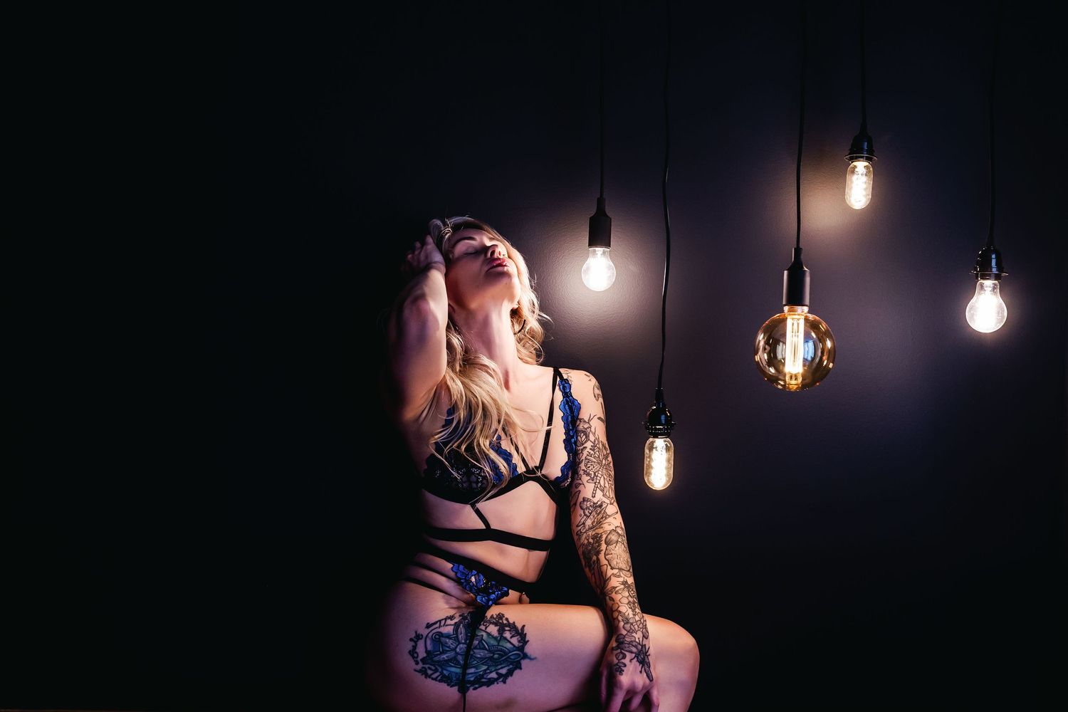 Moody boudoir portrait with hanging light bulbs creating atmospheric lighting.