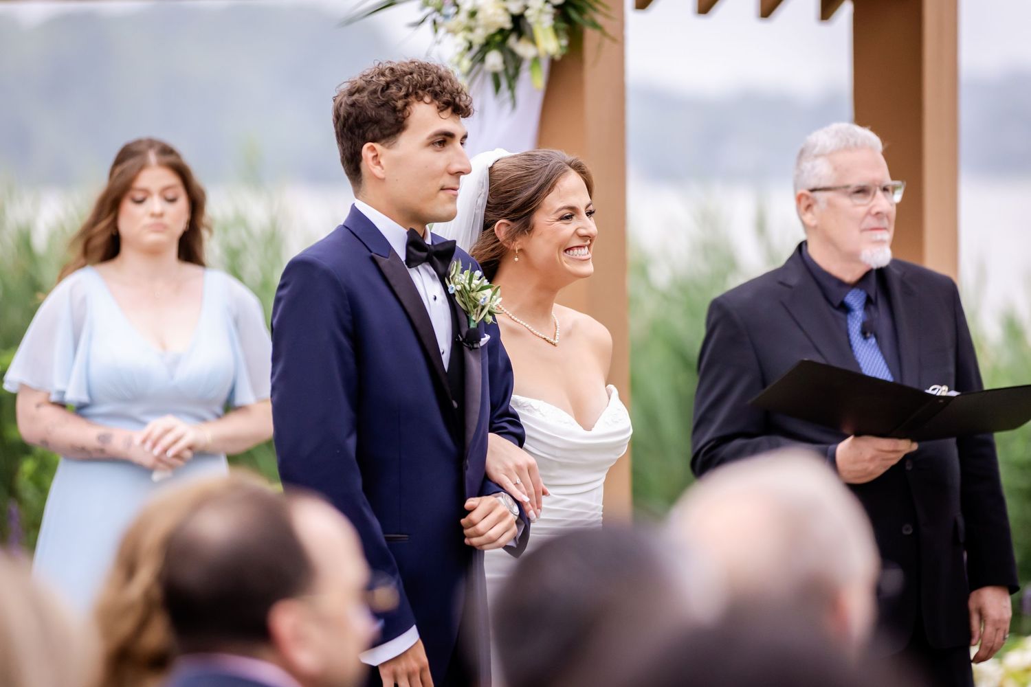 Wedding guests and wedding party members gather under a covered outdoor ceremony space.