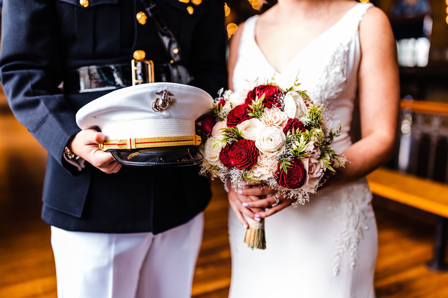 A wedding bouquet featuring burgundy and ivory roses with greenery at an elegant indoor reception venue.
