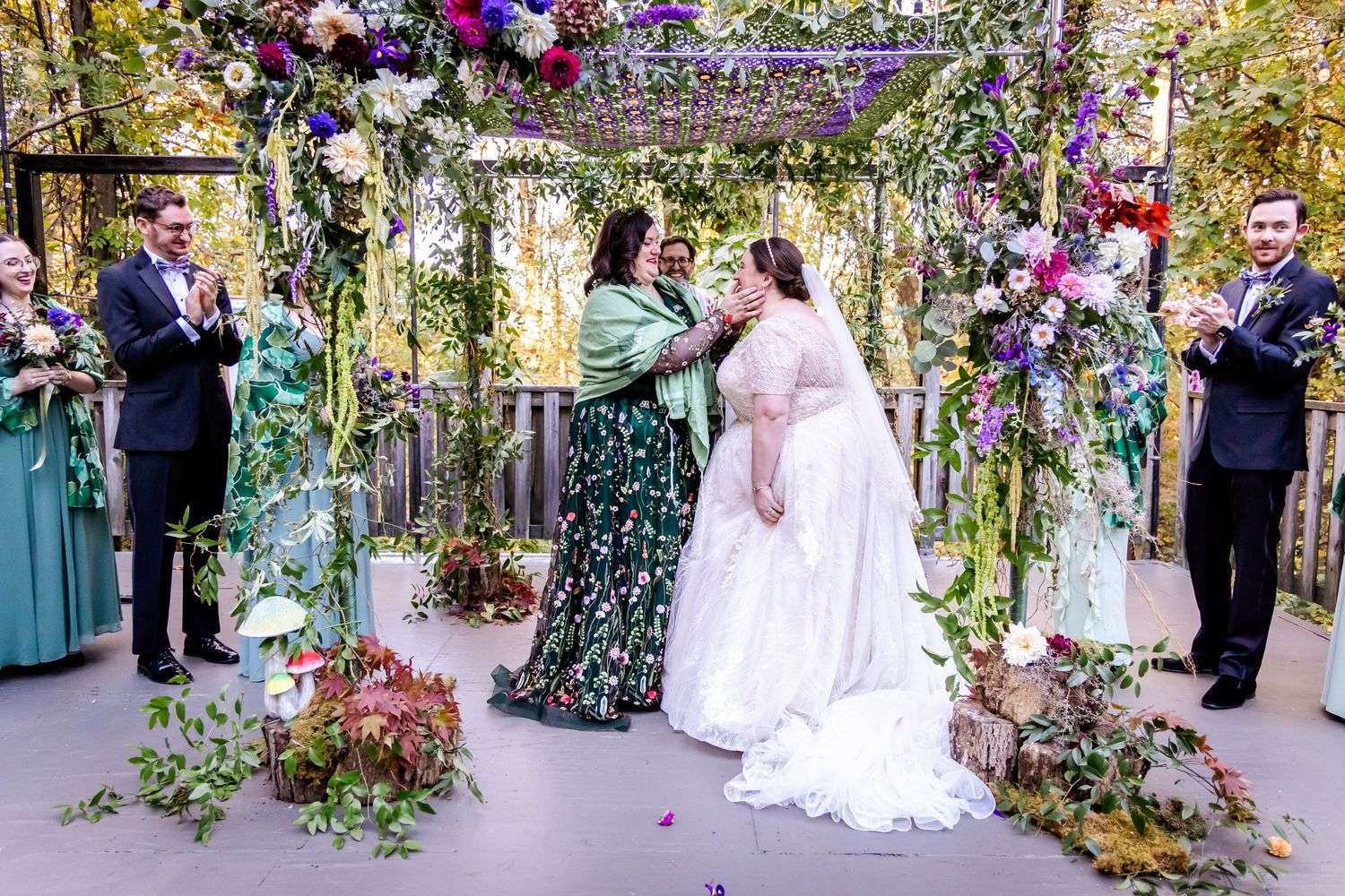 Wedding ceremony under floral arch with purple and pink flowers and greenery.