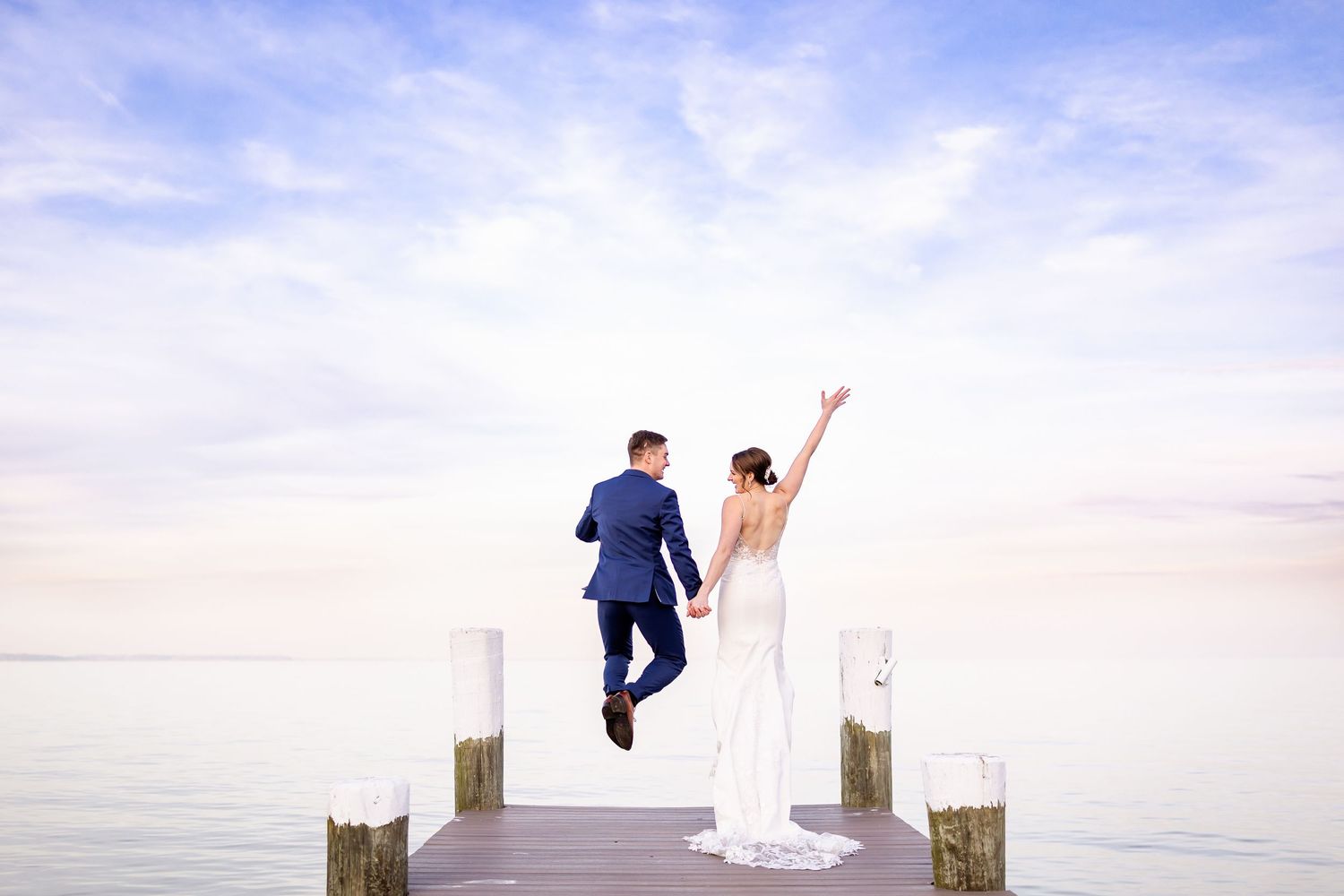 A couple poses on a wooden pier overlooking calm waters at sunset.