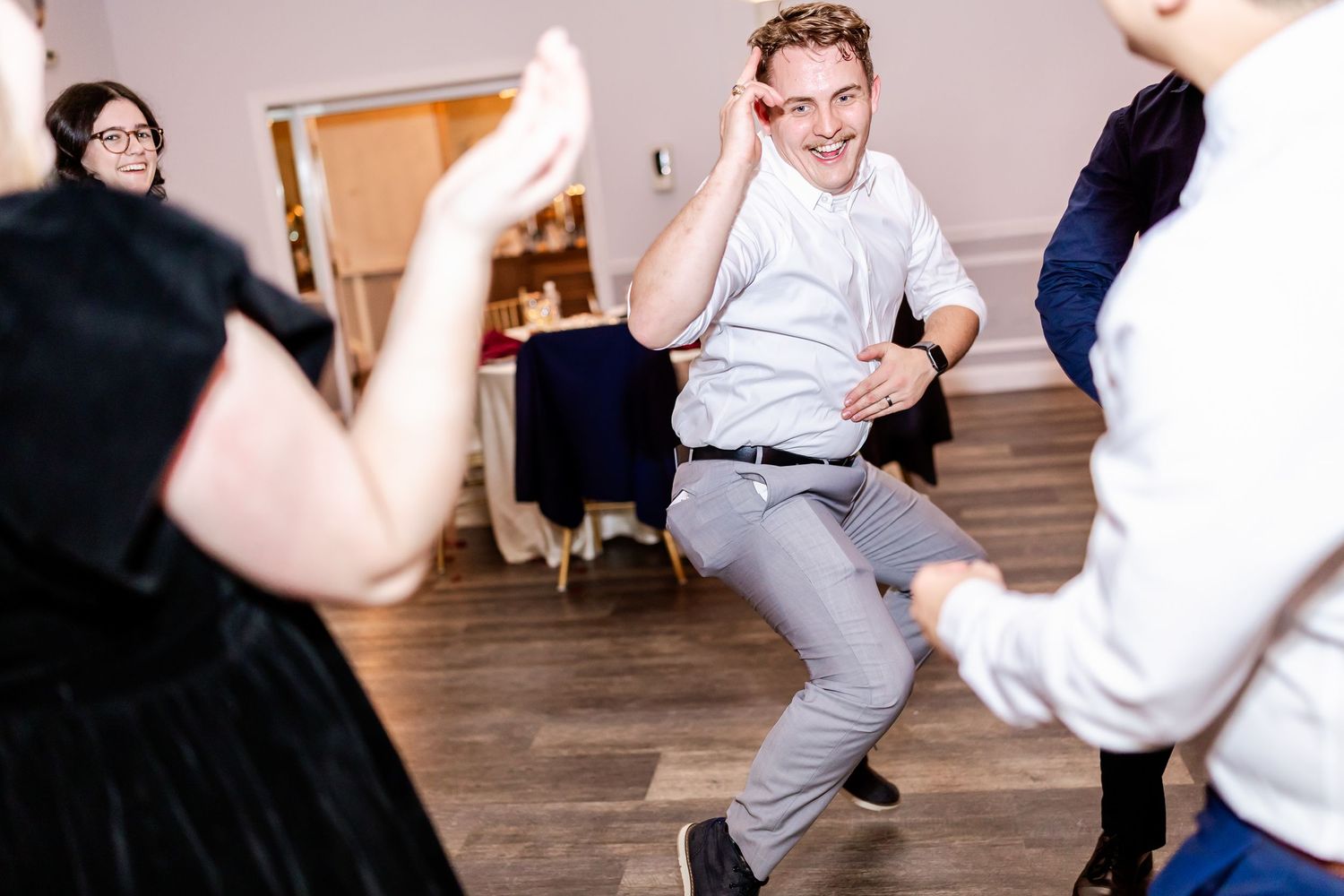Wedding guests dancing and celebrating on wooden dance floor at reception.