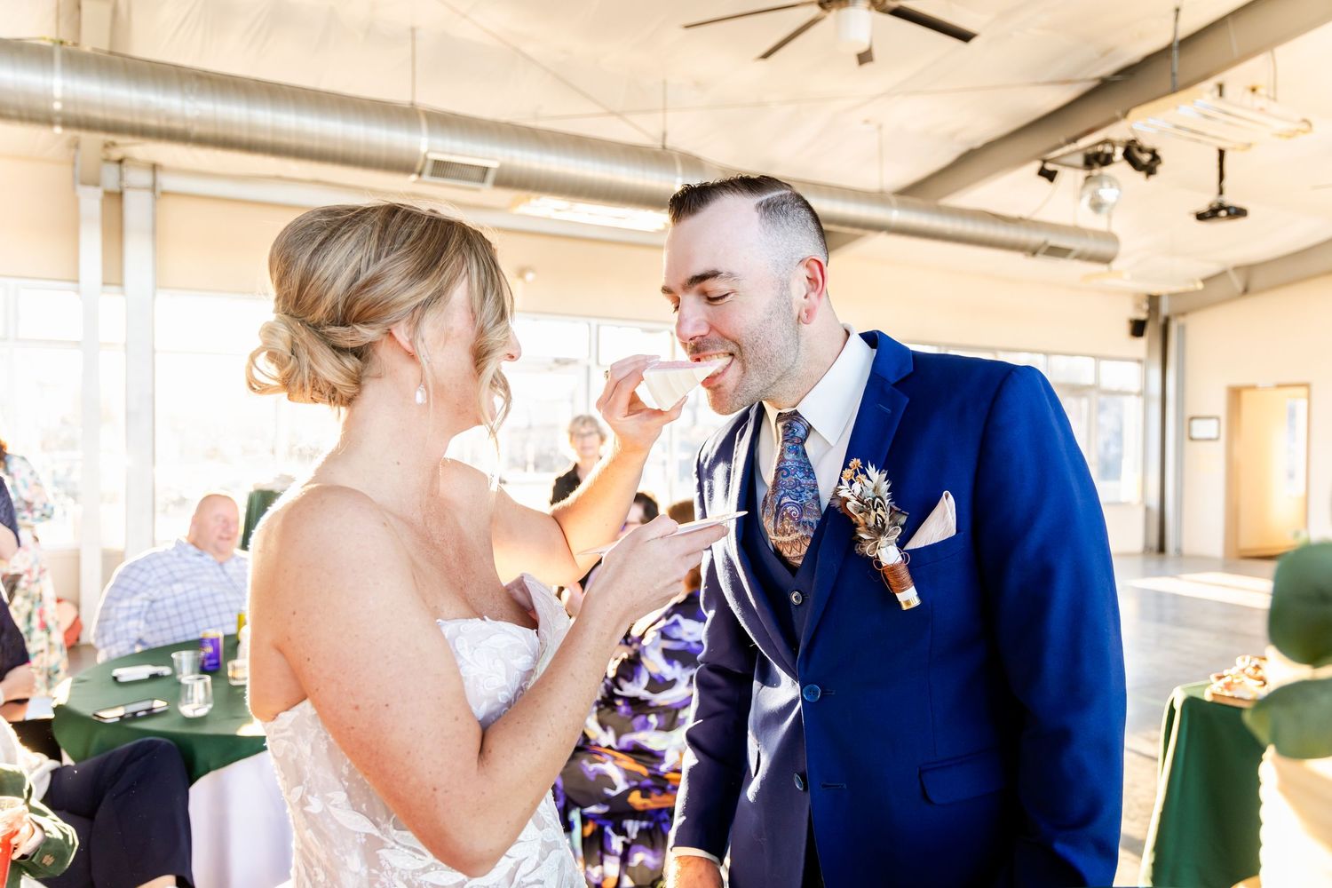 A couple shares a playful cake-feeding moment at their wedding reception.