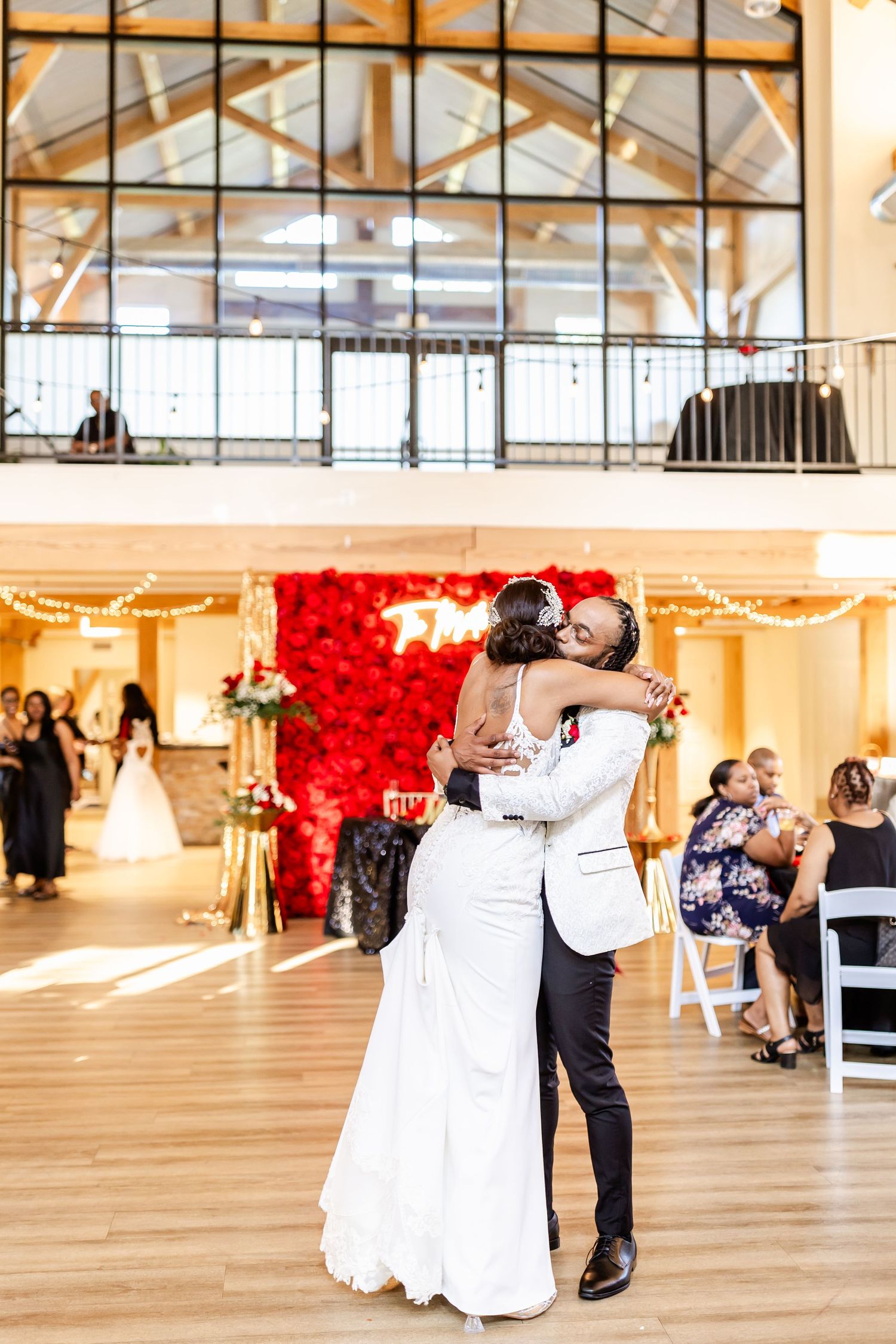 Intimate dance moment at wedding reception with red rose wall and high ceiling windows.