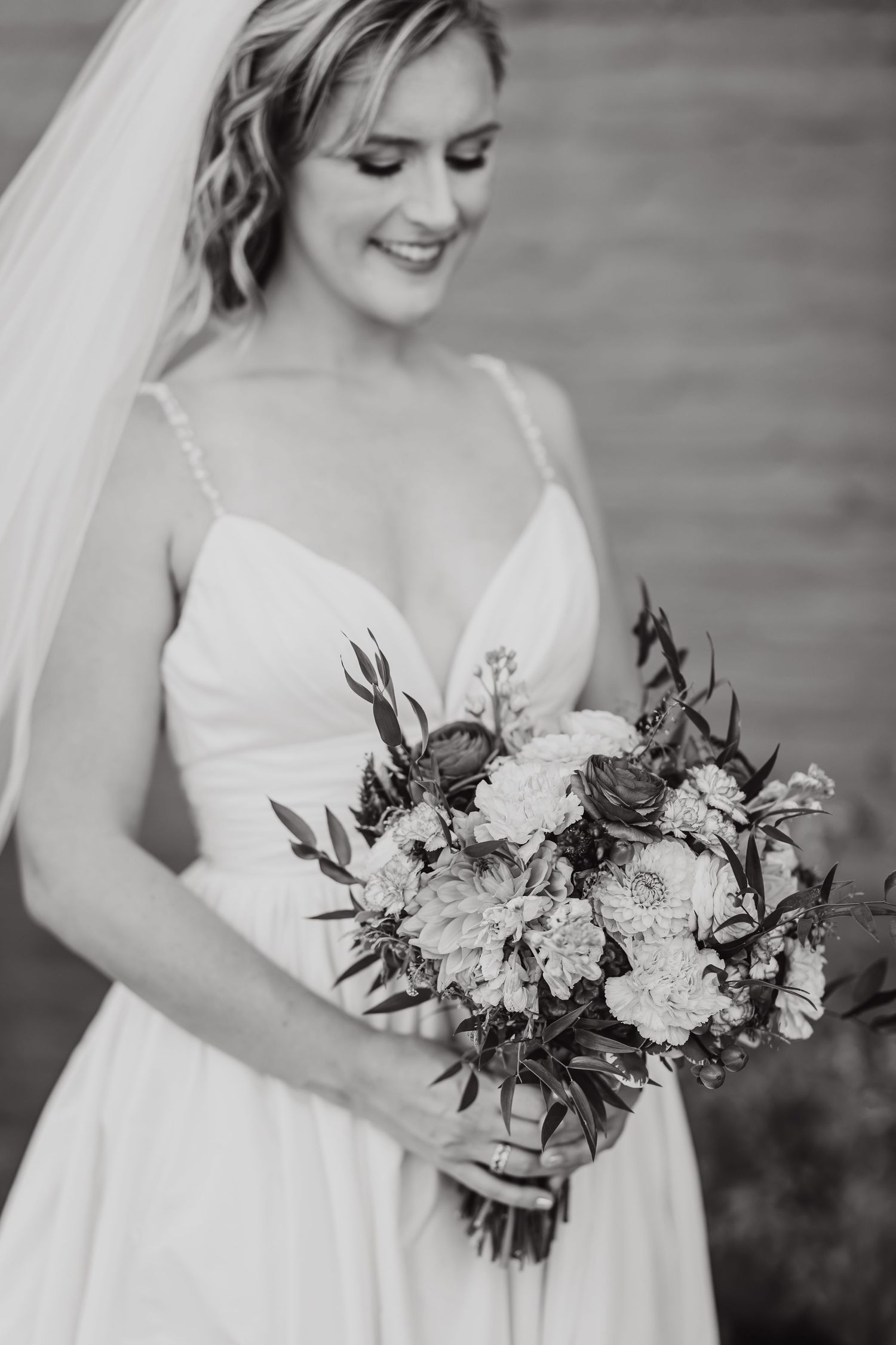 Black and white portrait of a bride in a white wedding dress holding an elegant floral bouquet.