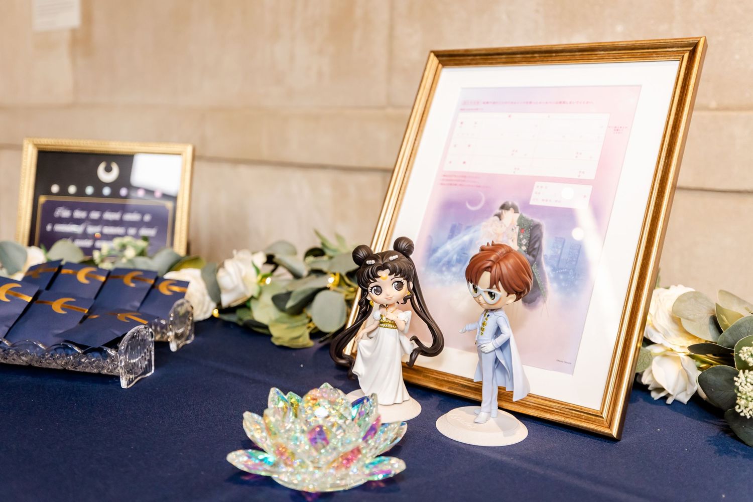 Wedding memorabilia display with anime figurines and framed artwork on navy blue tablecloth.