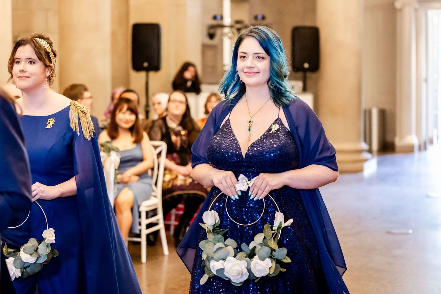 Bridesmaids in navy blue dresses carry white floral bouquets while walking down the aisle at an elegant wedding ceremony.