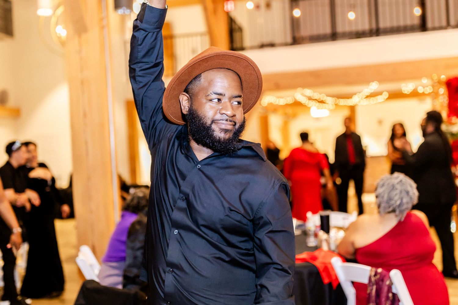 Guest in brown hat and black jacket dancing enthusiastically at wedding reception.