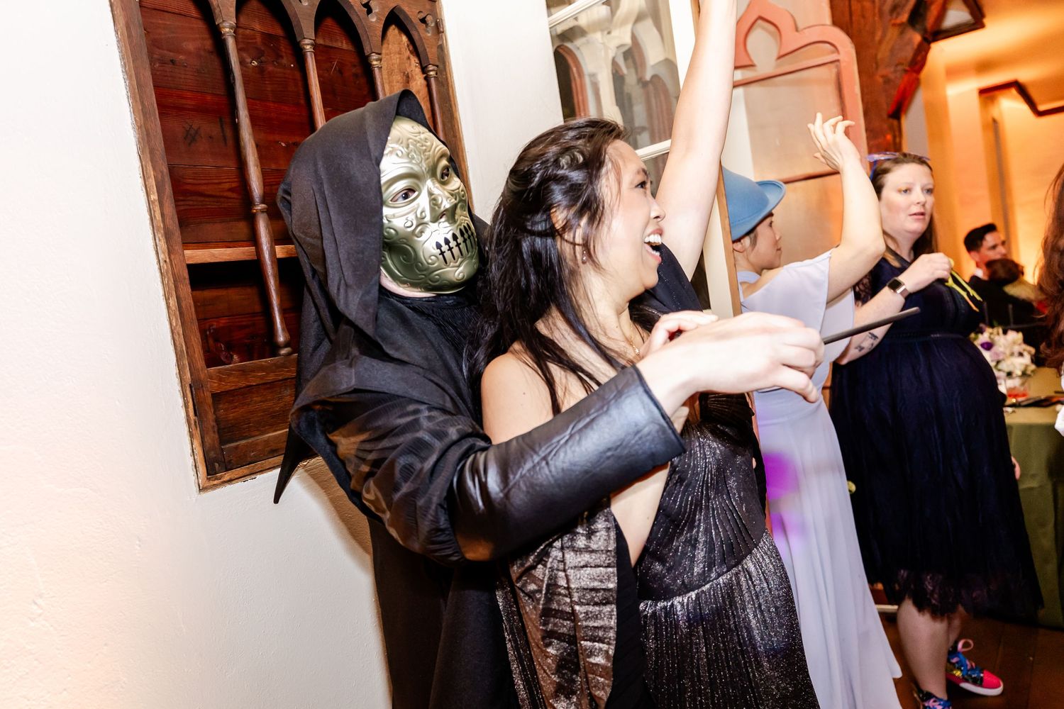 Party guests dance energetically as someone in a skeleton mask joins in at an indoor celebration.