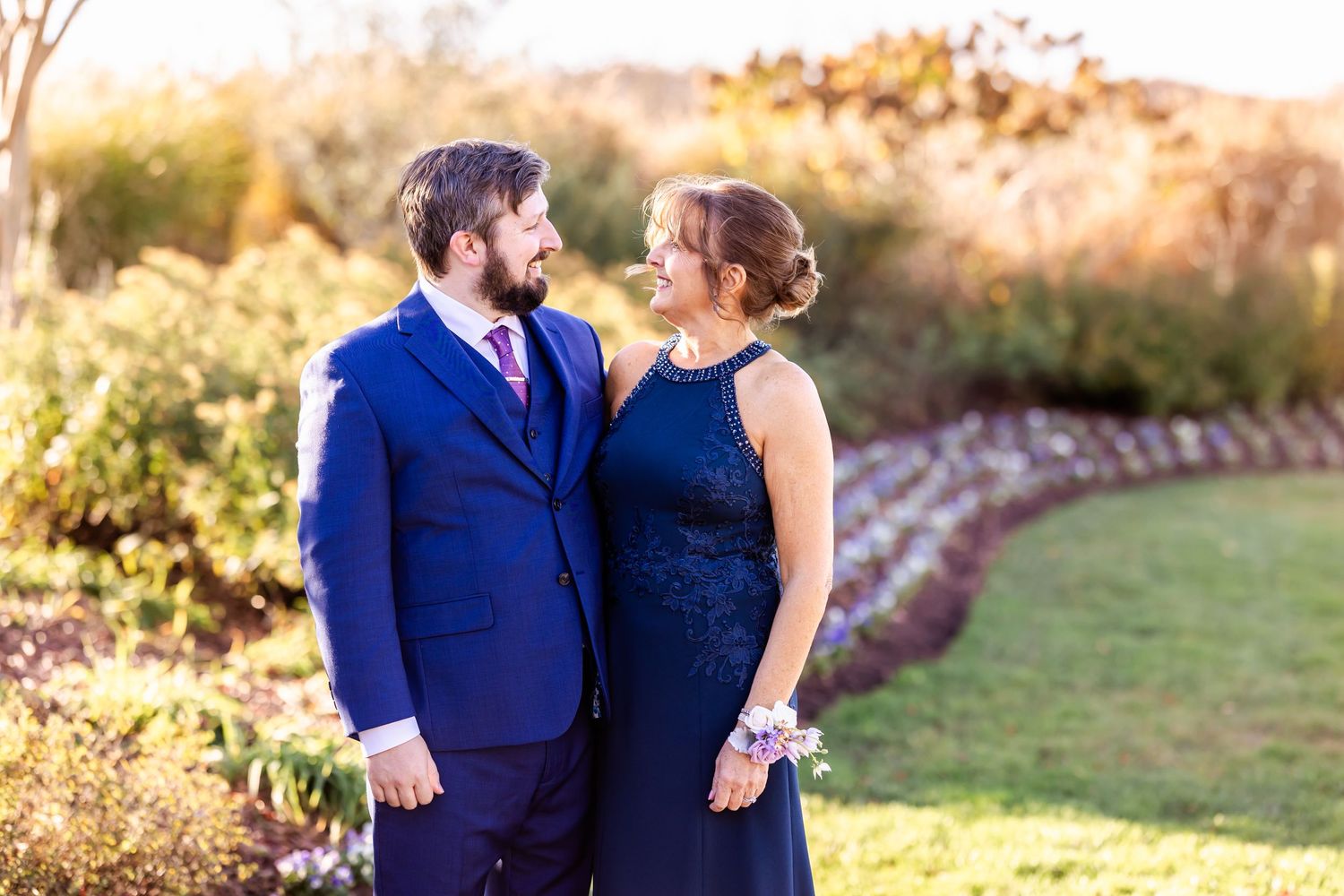 Couple in formal attire poses during golden hour in garden setting.