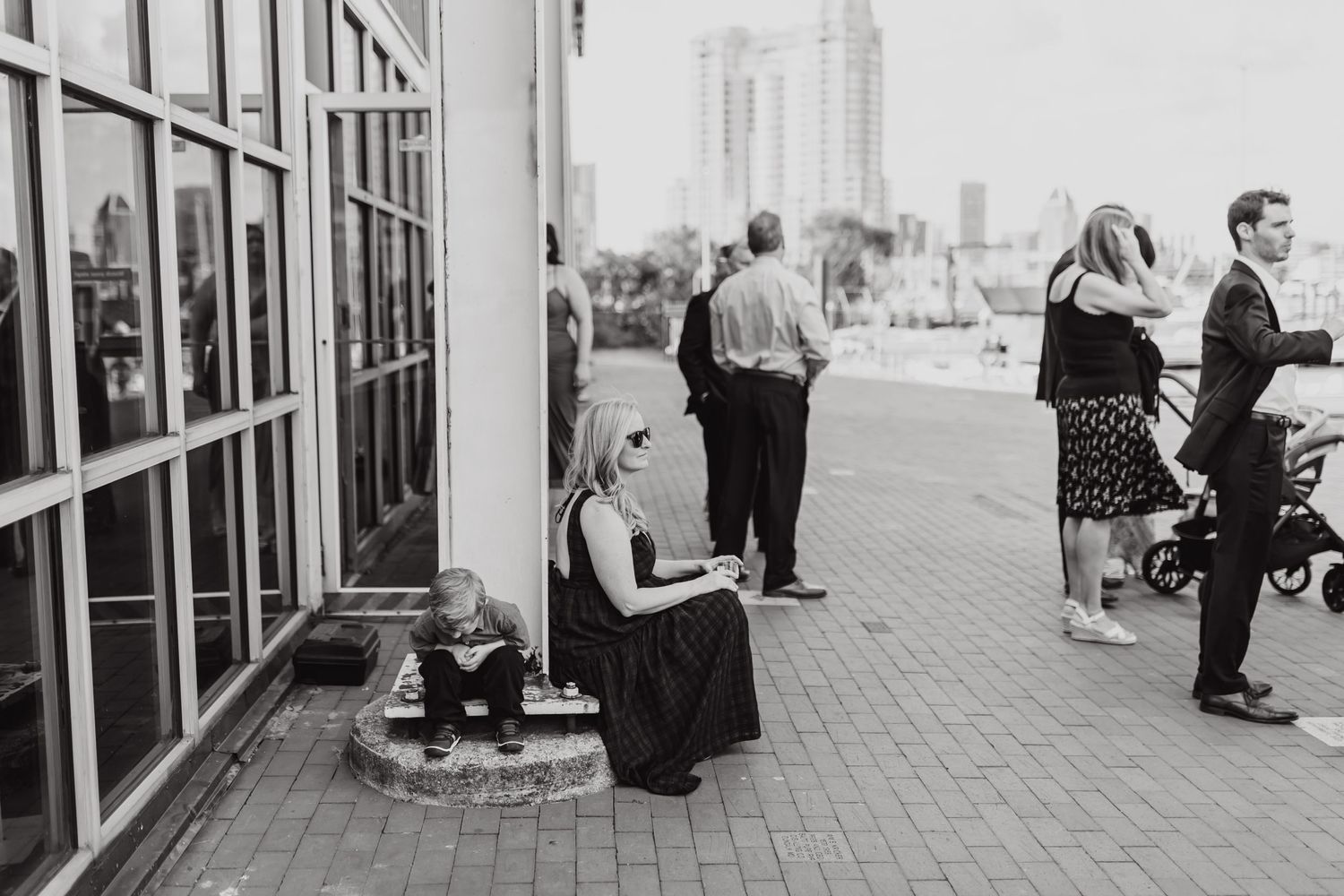 Black and white photo of wedding guests mingling outside urban building with city views.