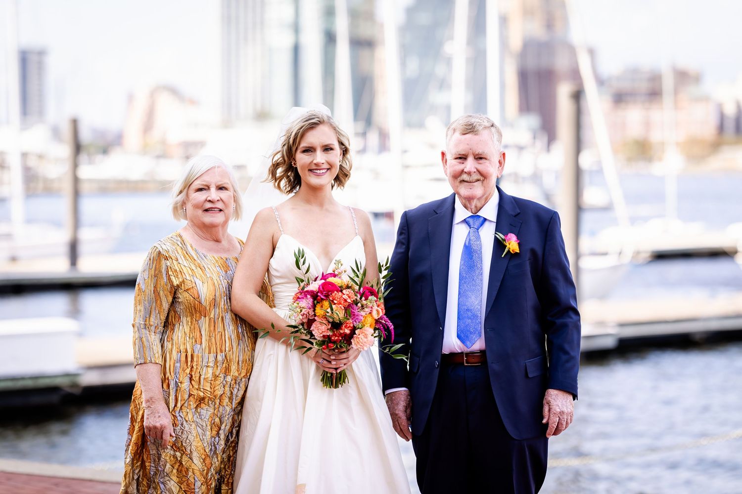 Wedding party posing together at Baltimore's Inner Harbor with city skyline and boats in background.