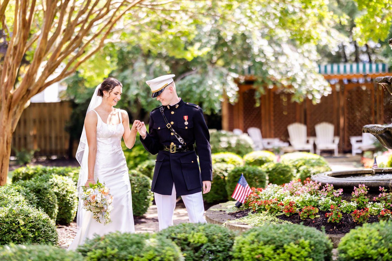 A bride and Marine in dress uniform walk together through a lush garden path during a wedding ceremony.