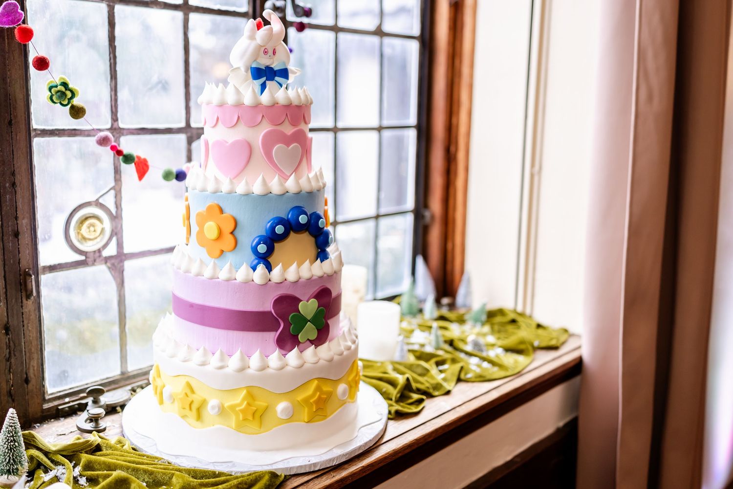 Colorful wedding cakes on display in a bright sunlit room with windows and elegant decorative details.