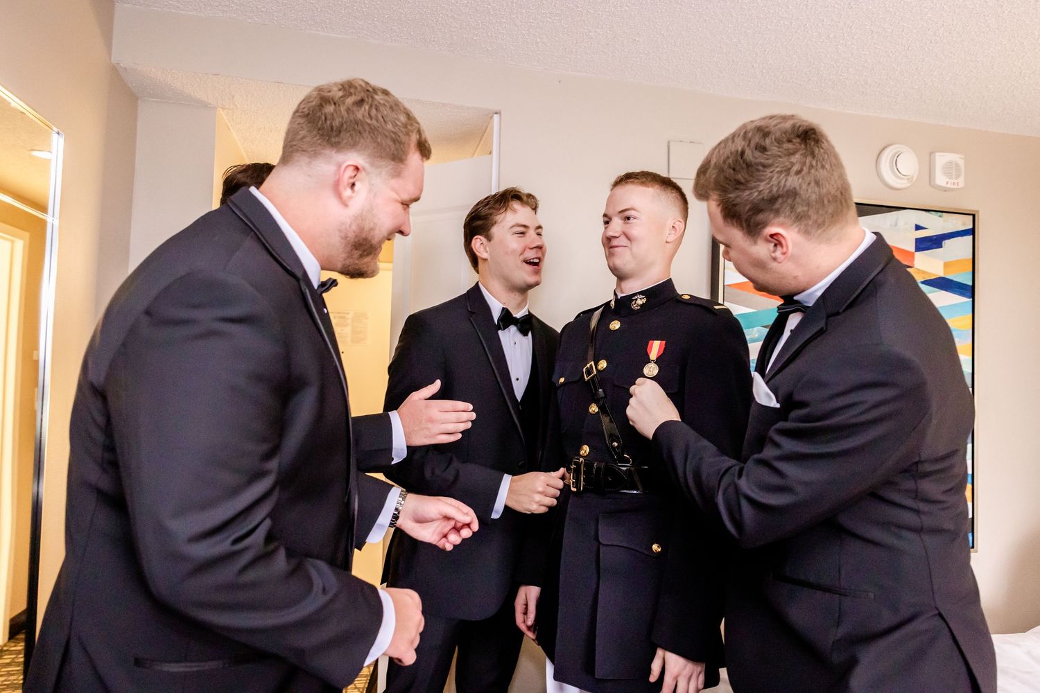 Groomsmen share laughs and celebrate in a hallway before a wedding ceremony.