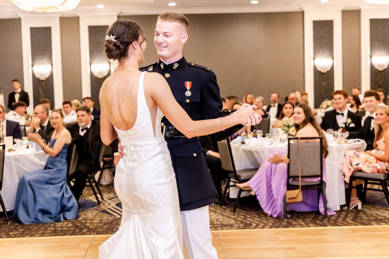Elegant ballroom wedding dance with formal attire and reception guests in background.