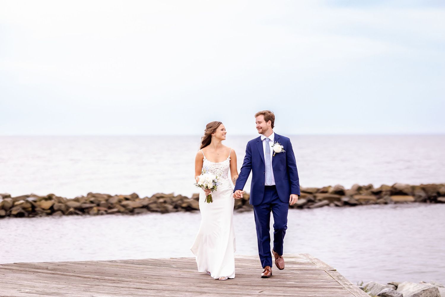 Wedding couple walking along a beachside boardwalk in formal attire.