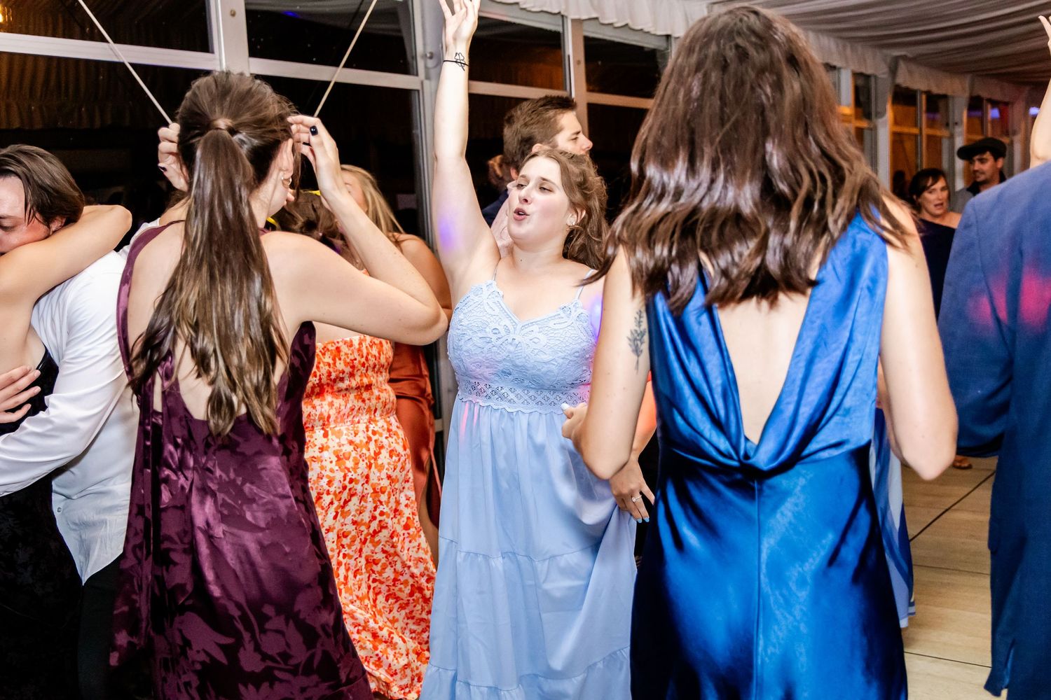 Wedding guests dancing in colorful dresses at an evening reception celebration.