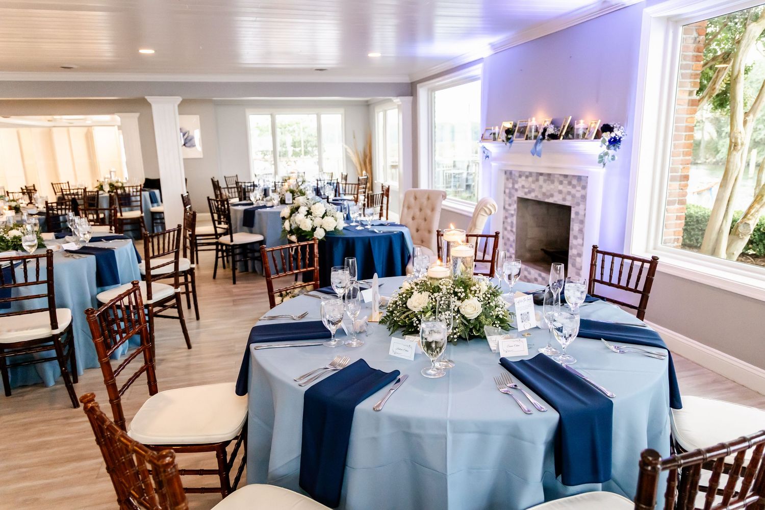 Elegant wedding reception setup with navy and white table decor, wooden chairs, and a fireplace centerpiece.