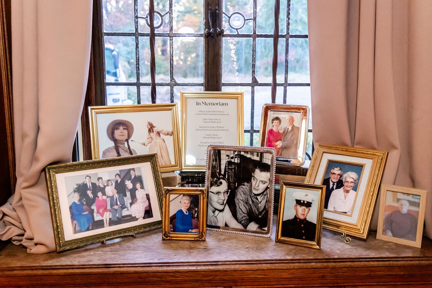 A collection of framed family photographs and memorabilia arranged on a wooden windowsill.