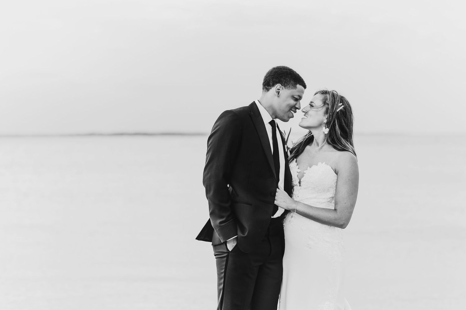 A romantic black and white portrait of a bride and groom embracing against a minimalist background.