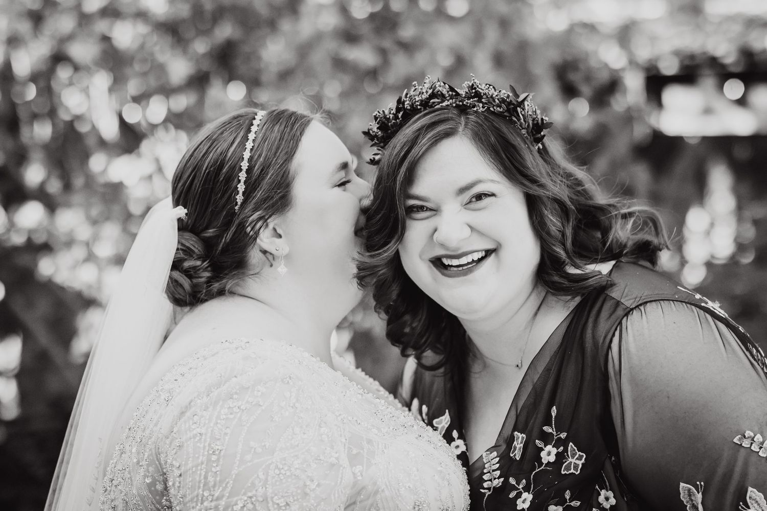 Black and white candid portrait of two wedding attendees sharing a joyful moment.