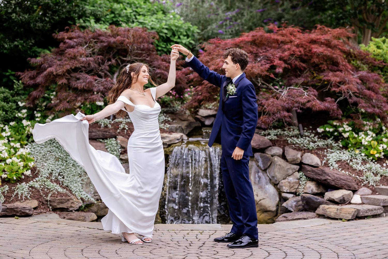 A couple dances together in a romantic garden setting with Japanese maple trees and stone walls.
