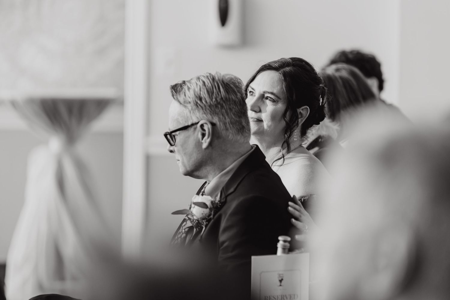 Candid black and white photo capturing emotional moments between wedding guests at reception.