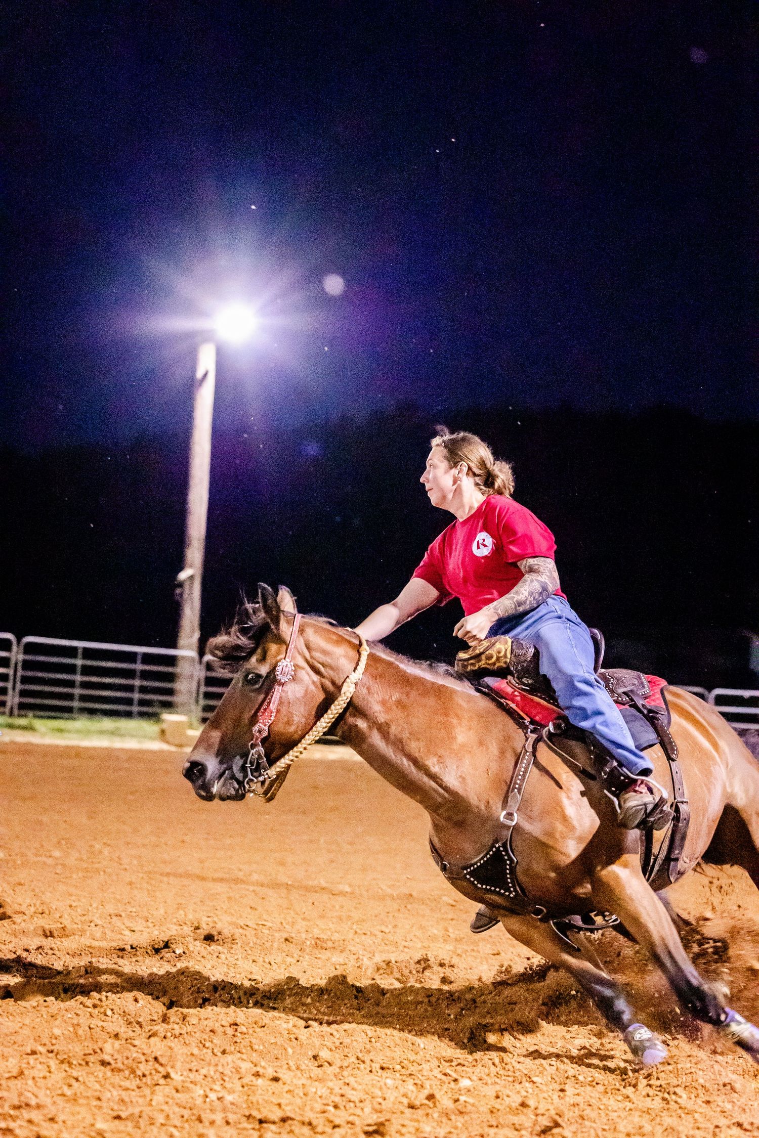 Rider on horseback competing in western-style barrel racing event at night.