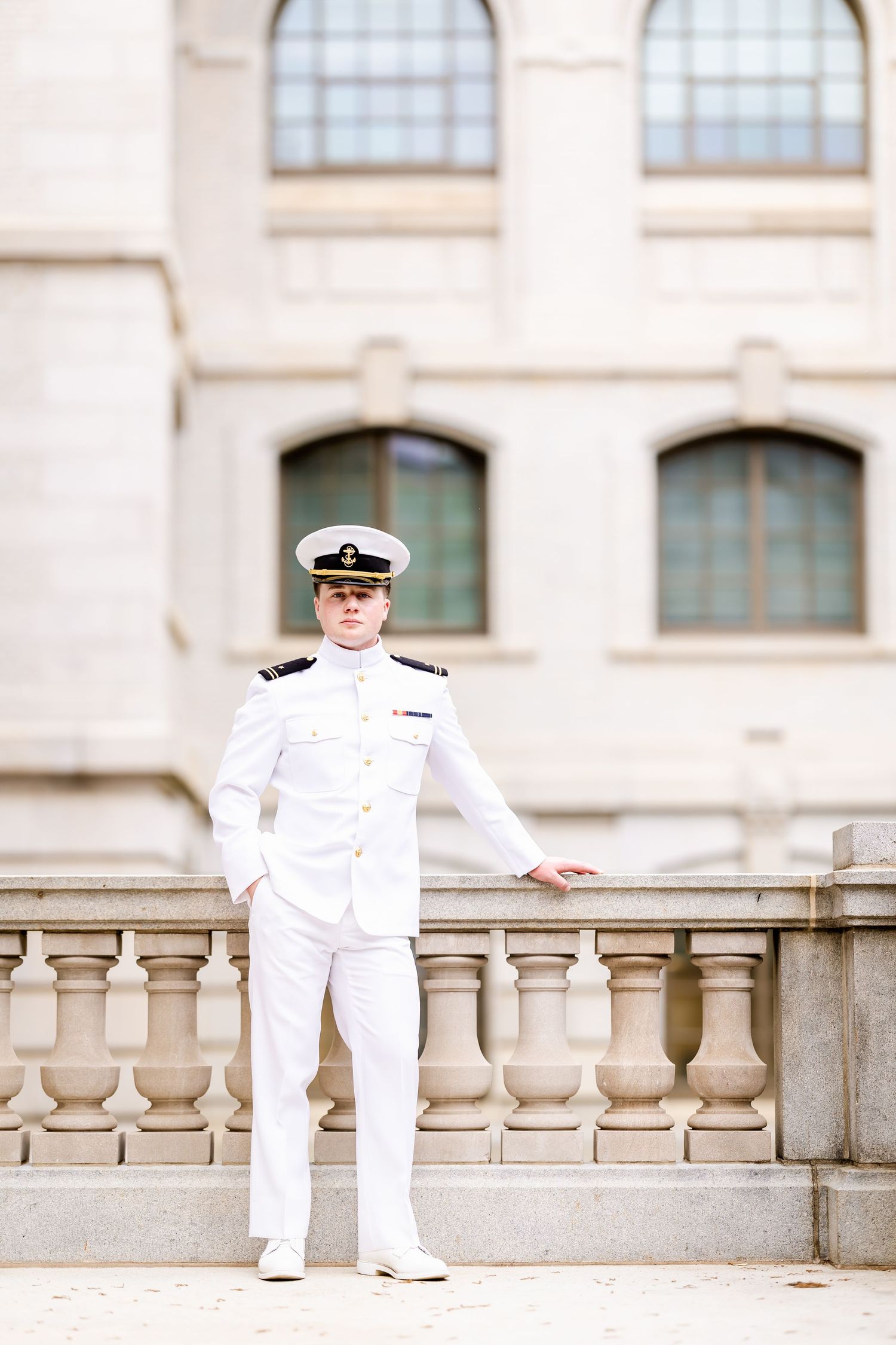 Naval officer in dress whites poses on classic stone balcony with architectural details.